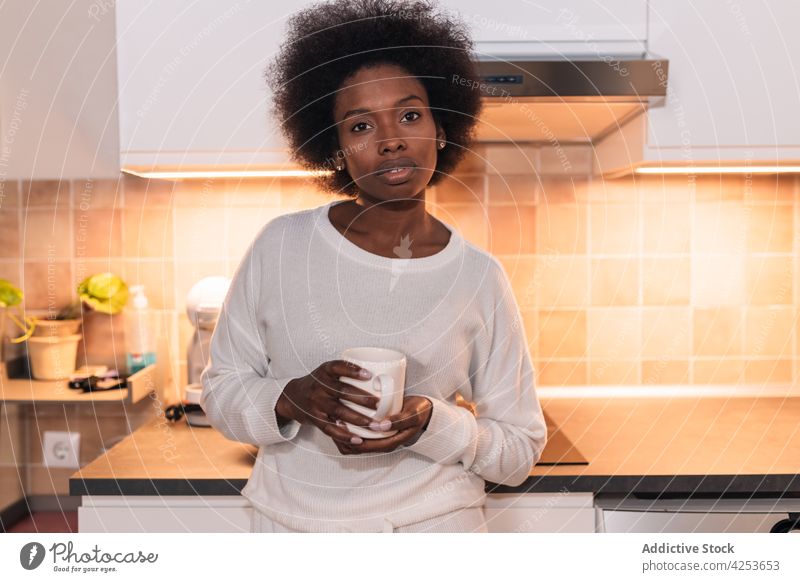 Calm young African American woman drinking coffee in kitchen serious calm beverage breakfast caffeine refreshment home awake female african american black