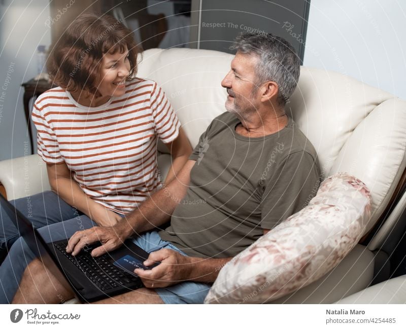 Smiling middle aged couple sitting on their couch using the laptop to buy online at home family woman computer shopping e-commerce internet technology