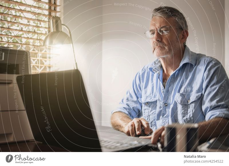 A senior man sitting at a desk in front of a laptop computer business technology crypto trade finance person block chain chart shopping book internet office