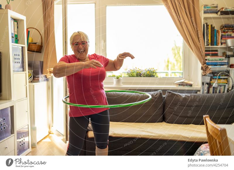 Older woman hula hooping at home eyeglasses wrinkles natural real people casual day lifestyle grandmother pensioner aged leisure retirement retired one person
