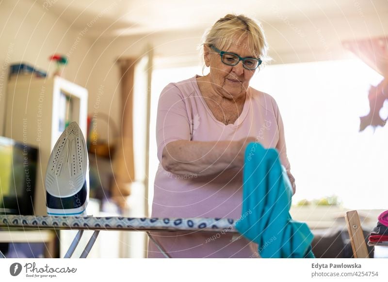 Senior woman at home ironing clothes eyeglasses wrinkles natural real people casual day lifestyle grandmother pensioner aged leisure retirement retired