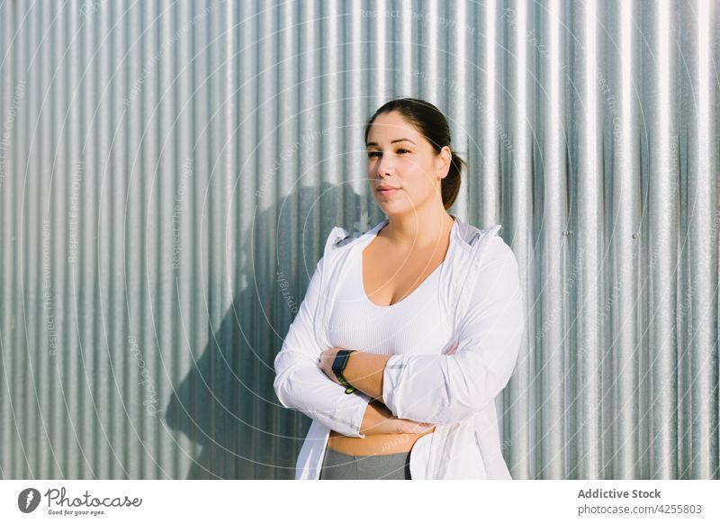 Young ethnic woman standing near metal wall after successful workout training wellness wellbeing confident healthy delight city street female young obese