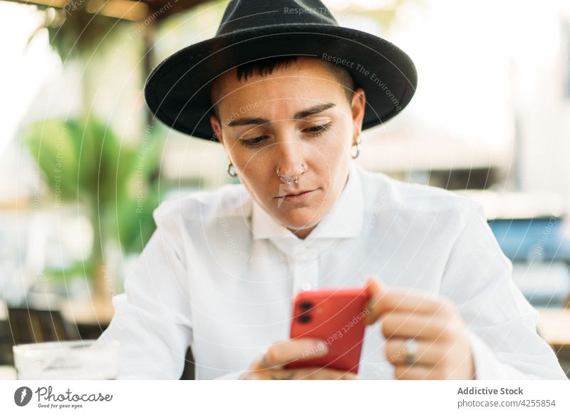 Pensive tomboy with smartphone in cafe woman transgender eccentric identity queer style agender serious device think white shirt weird unique accessory accept