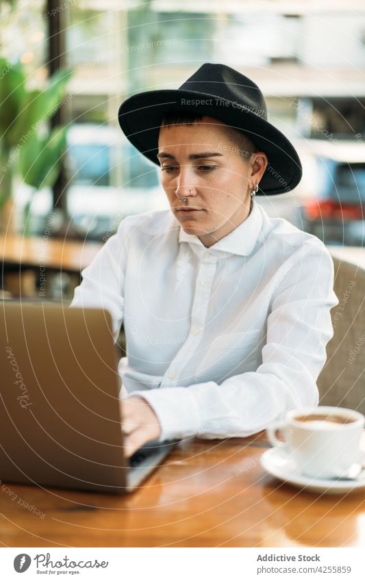 Stylish tomboy typing on laptop while working in cafe woman using freelance queer masculine browsing remote female surfing device netbook internet focus