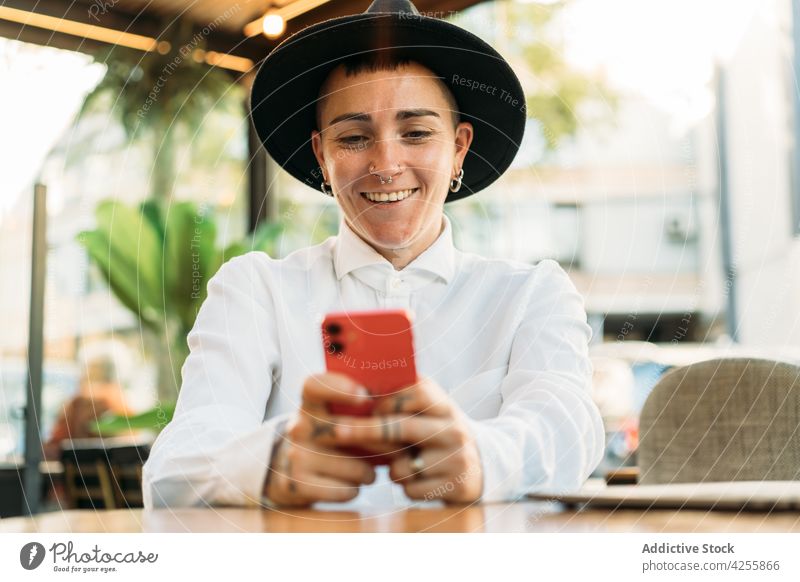 Glad tomboy with smartphone in cafe woman transgender happy eccentric cheerful identity smile queer style agender device think white shirt unique accessory