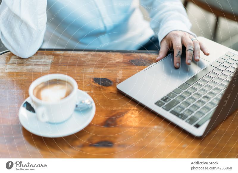 Person typing on laptop sitting at table with coffee person teleworker using freelance internet latte cup surfing busy online device gadget startup browsing