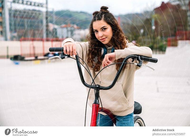 Positive woman riding bicycle in urban park positive smile cheerful ride city activity happy female hoodie jeans hobby active modern denim contemporary leisure