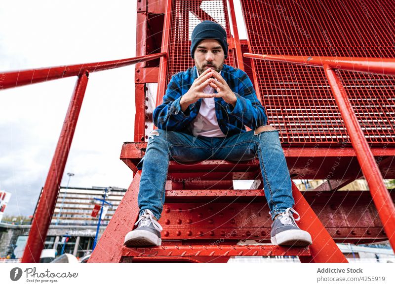 Man in trendy checkered blue shirt leaning on metal construction man checkered shirt confident casual outfit cool rest urban male hat contemporary weekend young