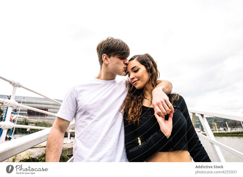 Loving young couple on pier of river water embrace embankment city relationship love happy hug together boyfriend urban railing girlfriend metal rest summer