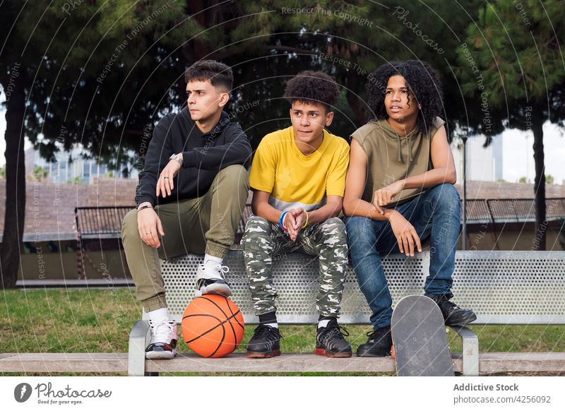 Multiethnic teenagers sitting on bench in park men friend attentive interest focus basketball together pastime skateboard male friendship young concentrate