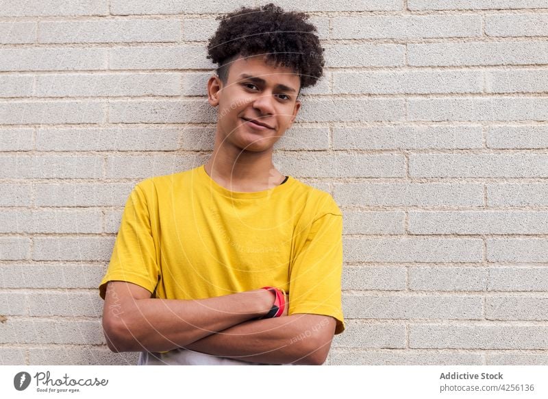 Smiling curly haired teen standing against brick wall man positive optimist cool posture cheerful youngster appearance male pleasant glad casual afro happy