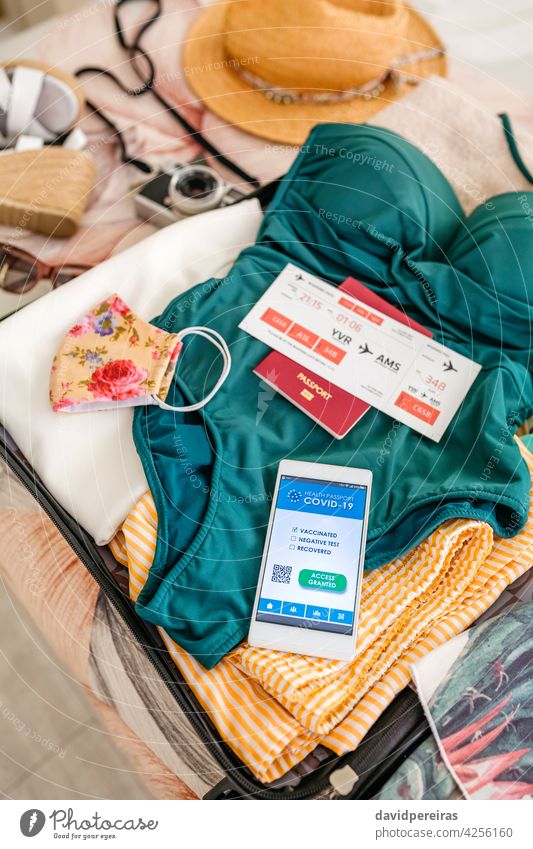 Open suitcase with woman luggage for beach vacation and covid passport top view woman suitcase swimsuit digital health passport holiday open suitcase