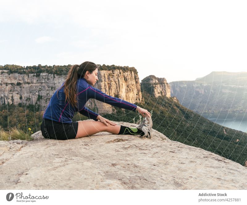 Young ethnic woman resting on rocky cliff after training in mountains stretch workout athlete nature concentrate wellness activity healthy female young hispanic