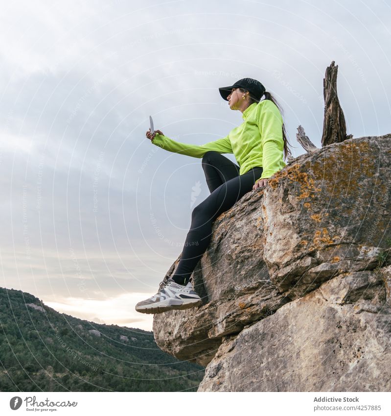 Traveling woman shooting mountainous landscape from rocky cliff take photo smartphone travel canyon hiker river viewpoint tourism nature female young casual