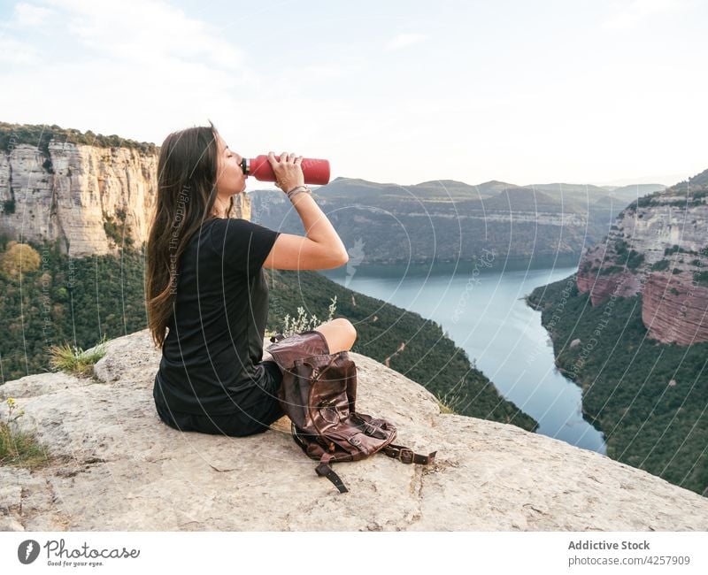 Young lady drinking water while recreating on rocky cliff during hiking trip woman mountain hiker trekking tired recreation river travel enjoy rest female young
