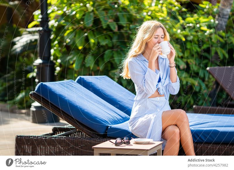 Smiling woman enjoying hot drink and sitting on deckchair toothy smile happy beverage chill carefree recreation resort sunbed relax summer content comfort