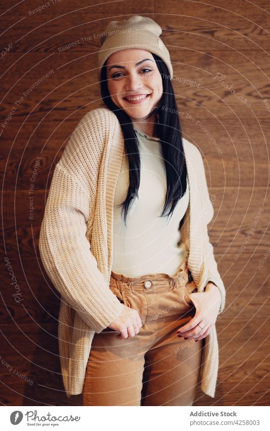 Smiling woman with hands in pockets on brown background smile sincere feminine hand in pocket gentle kind friendly charming portrait pleasant enjoy knitwear hat