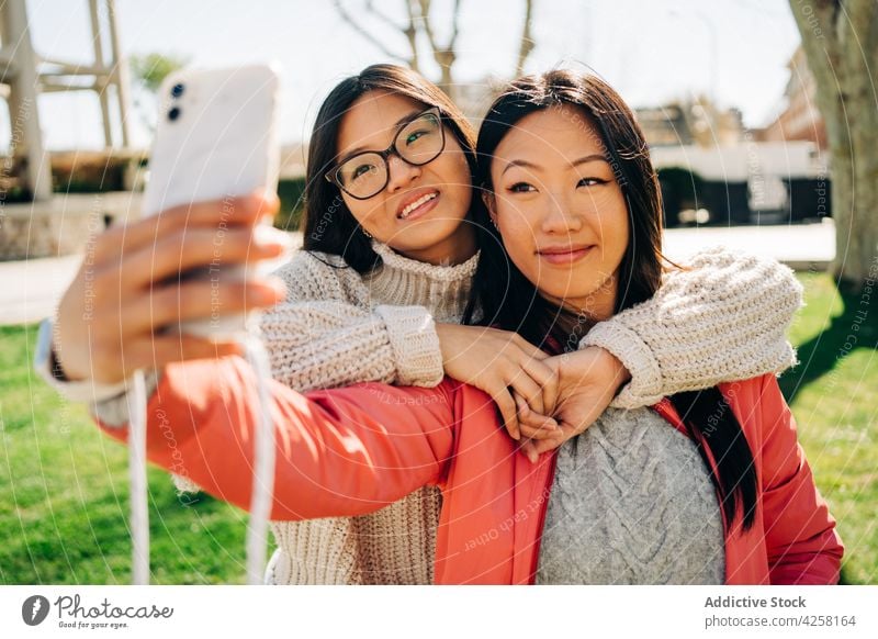 Delighted young Asian women showing peace sign while taking selfie in park smile smartphone friend v sign joy spend time cheerful mobile happy best friend asian