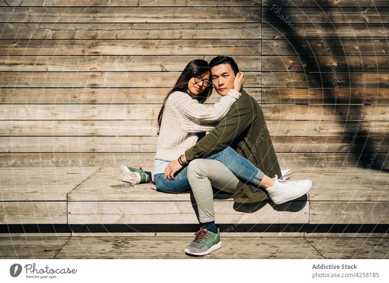 Beloved young ethnic couple cuddling on bench in park embrace together close affection relationship happy rest wooden smile boyfriend girlfriend asian dark hair