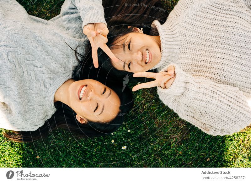 Young Asian ladies showing V sign and smiling while lying on grass in sunlight women smile lawn best friend cheerful v sign joy relax spend time free time