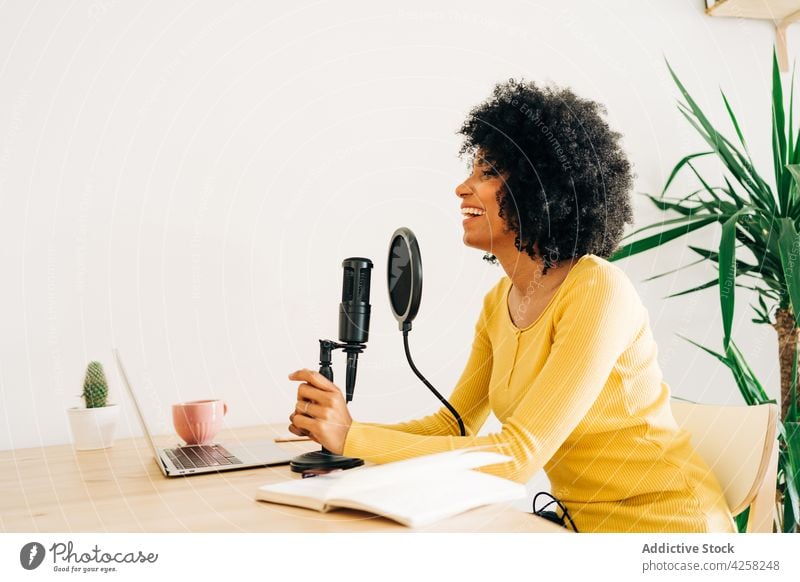 Positive young African American woman talking at online radio station podcast microphone laptop smile work positive record communicate broadcast social media