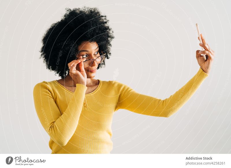Happy black woman in eyeglasses smiling and taking selfie happy smile positive smartphone mobile carefree female yellow sweater self portrait joy afro hairstyle