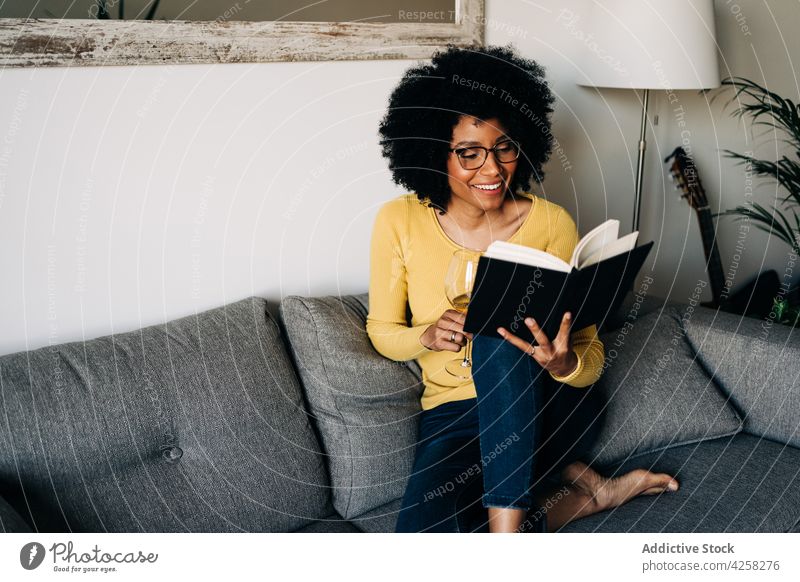 Delighted black woman with glass of wine and notebook delight smile glad home sofa cheerful relax female positive comfort couch weekend cozy african american