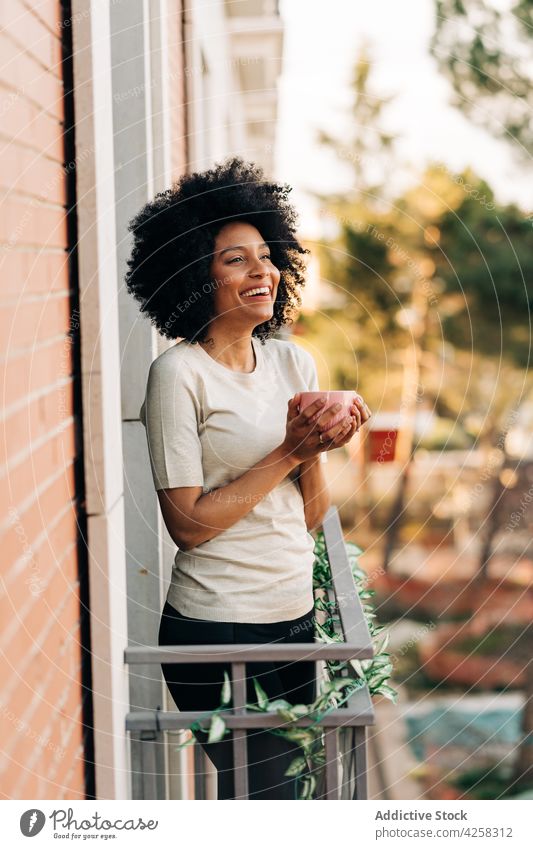 Relaxed black woman with hot cup of coffee on balcony relax smell hot drink smile fragrant happy street female enjoy african american dreamy ethnic city modern