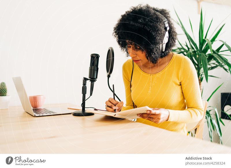 Young black lady writing notebook while recording podcast in studio woman write stream microphone work radio concentrate busy female focus young
