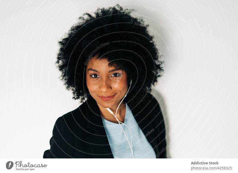 Positive black woman listening to music on earphones positive smile cheerful elegant suit smartphone happy female glad african american using optimist afro