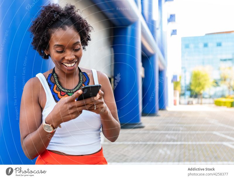 Joyful black woman using smartphone and walking on street joyful city cheerful stroll browsing device workout slim energy summer happy excited surfing mobile