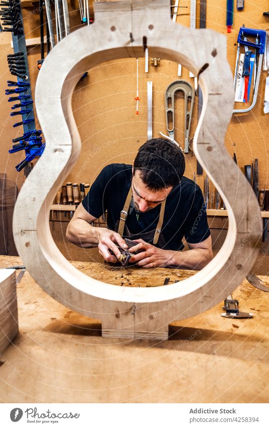 Focused artisan working with wood while building guitar flatten woodwork plane make instrument attentive man small business workroom craftsman musical