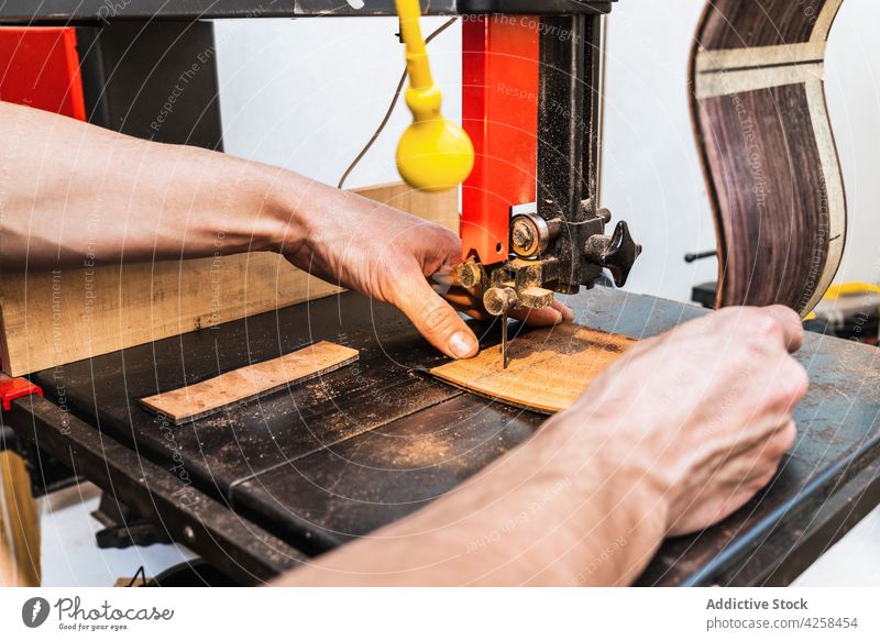Anonymous luthier cutting guitar body on bandsaw in workroom make craft woodwork workshop man small business professional musical machine instrument concentrate