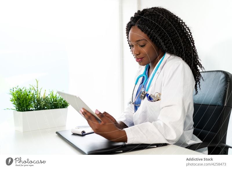 Smiling black woman in medical uniform using tablet in hospital doctor clinic medicine work health care busy female stethoscope practitioner specialist device