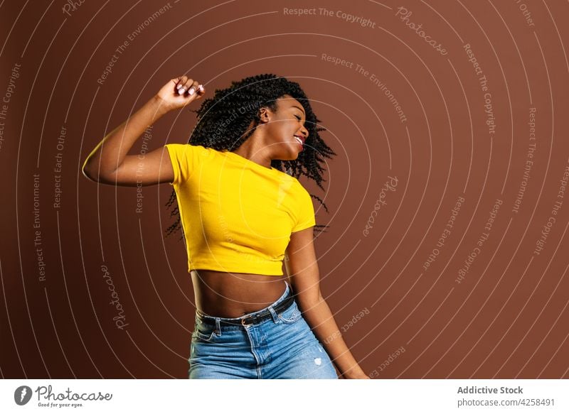 Smiling black woman raising hands while dancing positive dance move rhythm action motion leisure enjoy eyes closed cool female cheerful perform expressive music