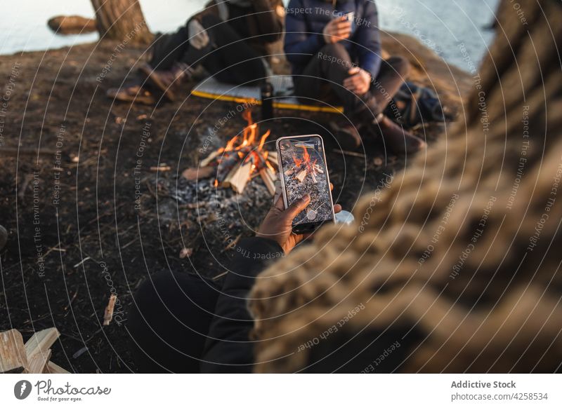 Anonymous black woman photographing fire during camping with friends people take photo smartphone camper bonfire traveler together spend time nature friendship