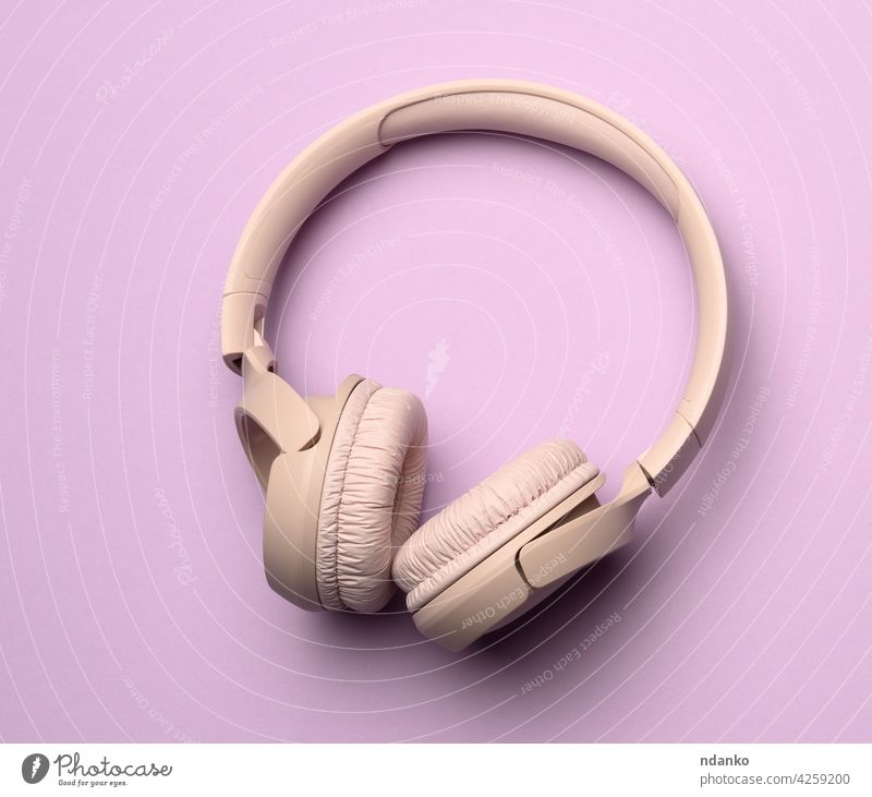 beige wireless headphones on a purple background equipment music personal stereo audio sound modern studio device technology headset digital listen