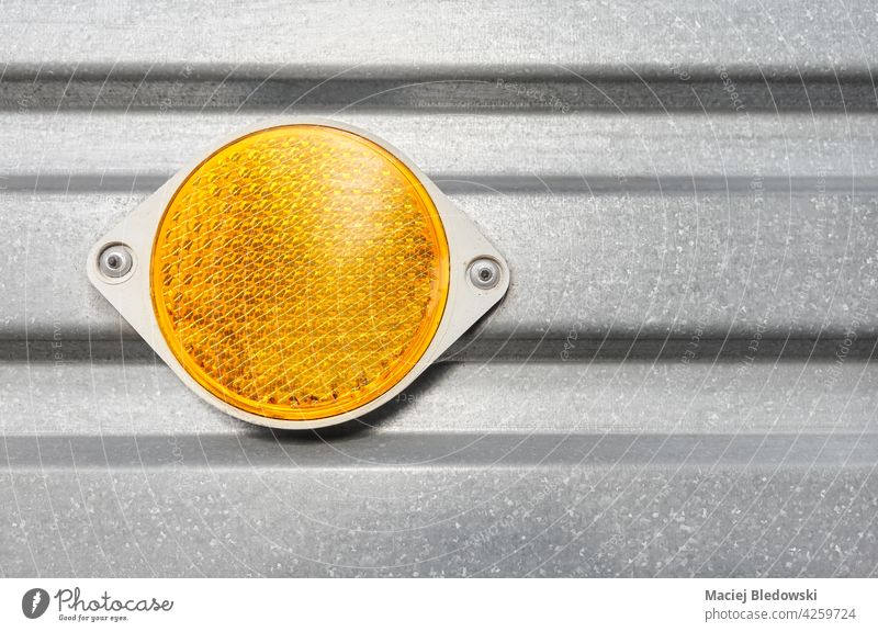Close up of a round plastic yellow reflector attached to a trailer corrugated metal side. reflective orange safety wall transportation silver background warning