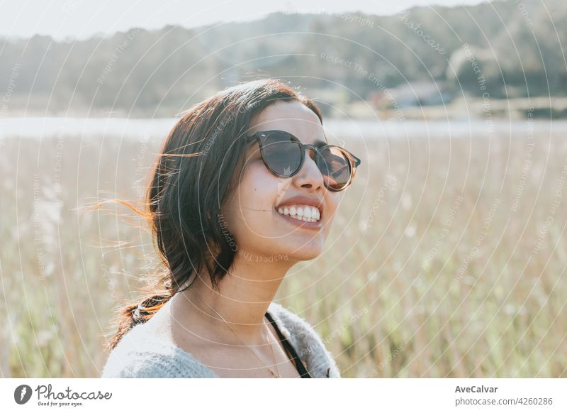 Woman using sunglasses smiling to camera while on the country yard during a super sunny day with copy space and lifestyle shot person carefree enjoying face fun