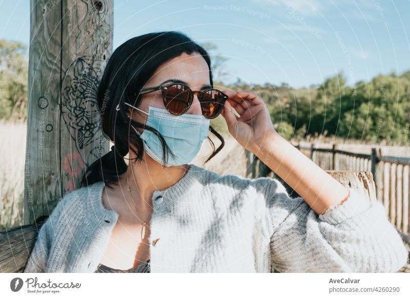 Woman using sunglasses and a face mask smiling to camera while on the country yard during a super sunny day with copy space and lifestyle shot person carefree