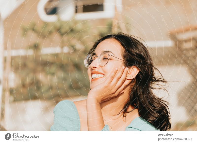 Young woman with glasses smiling to camera during a super sunny day with copy space lifestyle concept happy day person carefree enjoying face fun hair