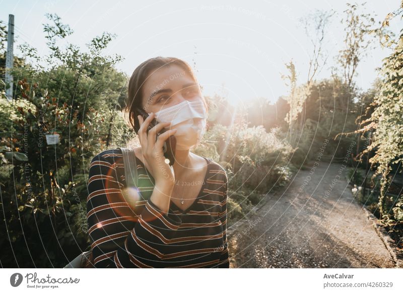 Young woman using a face mask making a call in a garden during a super sunny day copy space smiling social media phone caucasian female enjoy hipster horizontal