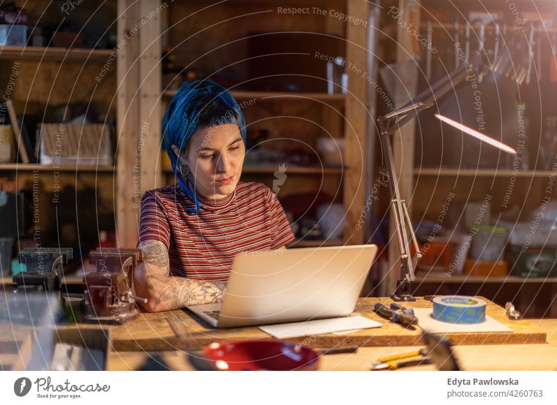 Young woman using laptop in her workshop diy hipster hair tattoos female owner profession service small business employee working workplace maintenance adult