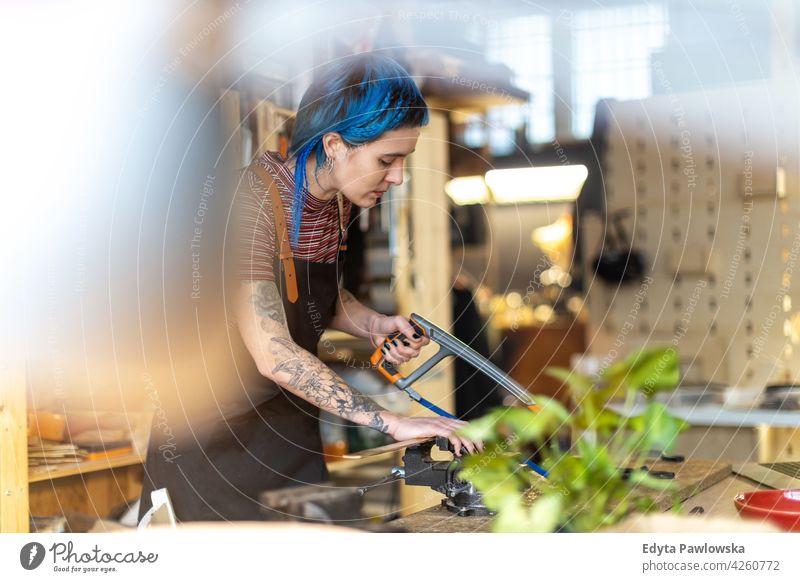 Woman using hand saw in her workshop diy hipster colorful hair tattoos woman female owner profession service small business employee working technician