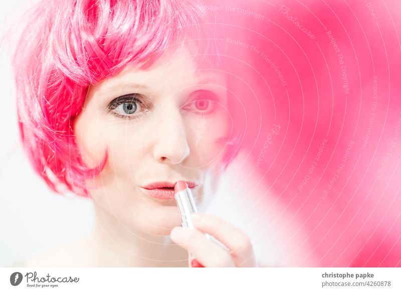 Woman in pink wig applies lipstick Wig Apply make-up Lipstick Hair and hairstyles Make-up Feminine Face Mirror Mirror image Cosmetics Young woman pretty Mouth