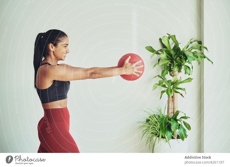 Smiling ethnic sportswoman exercising with fit ball outstretch exercise workout training practice content room smile vitality athlete fitness energy enjoy