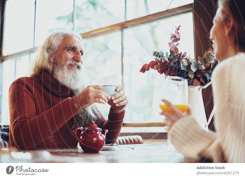 Cheerful man talking to unrecognizable partner in cafe speak friend tea hot drink friendly spend time happy table gather beverage breakfast elderly smile candid