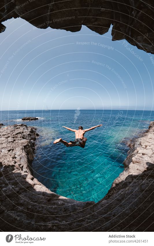 Back view of anonymous man jumping over sea ocean cave nature highland hole sky activity rebel mount rough endless horizon active seascape male dynamic alone
