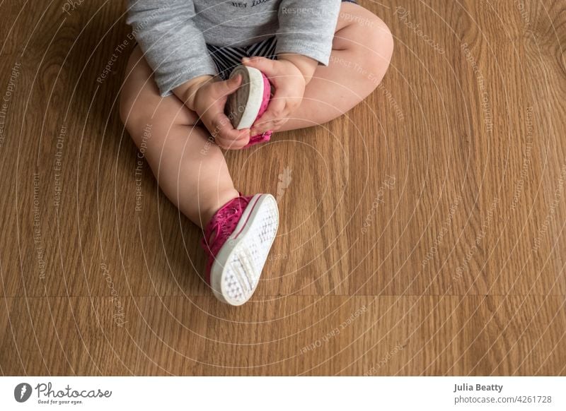 Young toddler baby holding foot with pink and white shoe on; exploring first pair of shoes first shoes sit seated feet together posture spine upright yoga