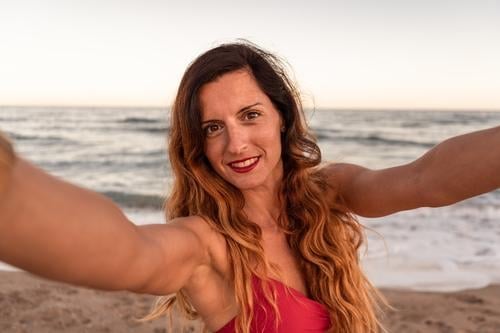 Pretty stylish woman having fun taking a selfie on beach at sunset. sea summer happy camera nature outdoor lifestyle use smartphone young adult cell phone